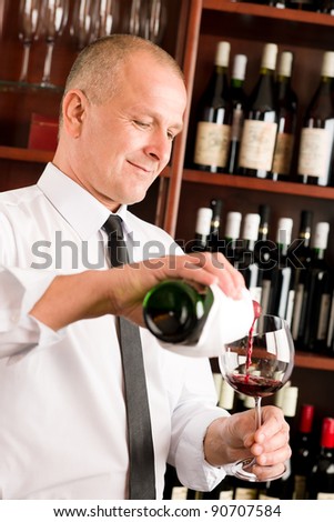 At the bar - senior barman pour red wine in glass