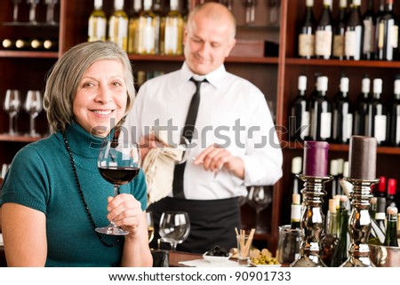 Wine bar senior woman enjoy wine glass in front of bartender