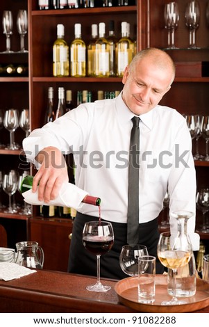 At the bar - waiter pour red wine in glass restaurant