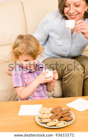 Little granddaughter with grandmother eat cookies drink tea cup together
