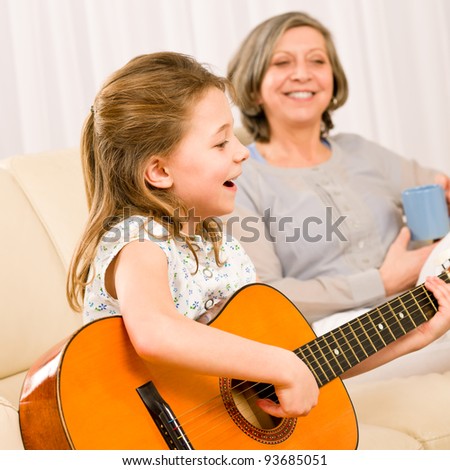 Young girl granddaughter sing play guitar to grandmother smile