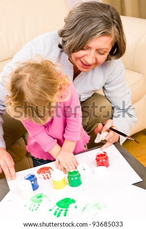 Grandmother with granddaughter playing together paint hand-prints on paper