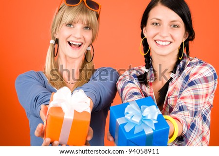 Two young woman friends hold party presents smiling orange background