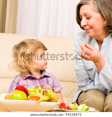 Little girl watch grandmother eat fruit relaxing on sofa