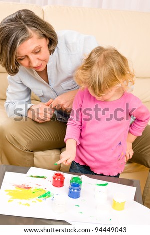 Grandmother with granddaughter playing together paint hand-prints on paper