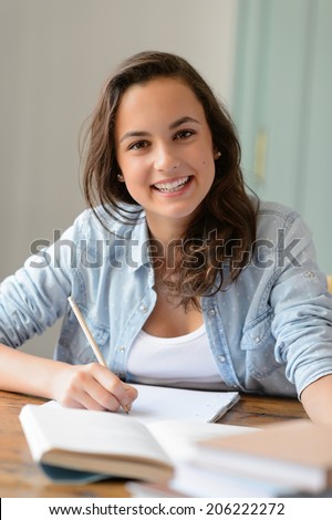 Teenage student girl studying at home smiling at camera