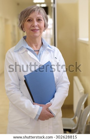 Senior doctor standing in hospital hallway holdings patient files