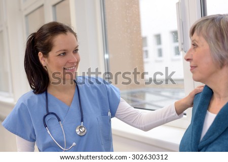 Smiling female doctor comforting senior patient in hospital corridor