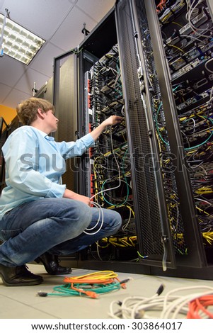 IT specialist installing cables in datacenter by open rack of patch panels