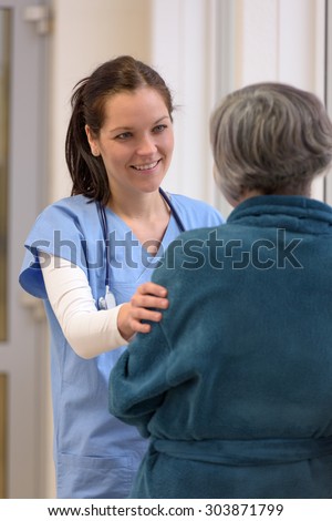 Smiling female doctor comforting senior patient in hospital corridor holding by arm