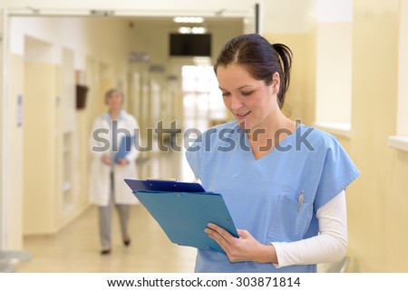Smiling young female nurse in hospital looking down at patient files