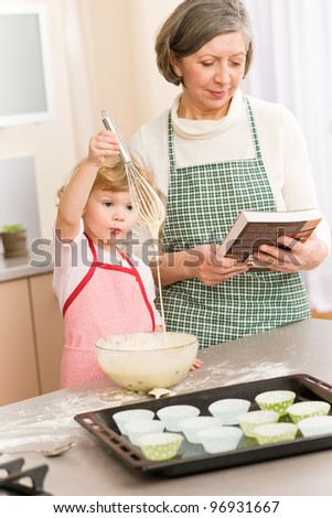 Funny little girl baking cupcake with grandmother hold whisk