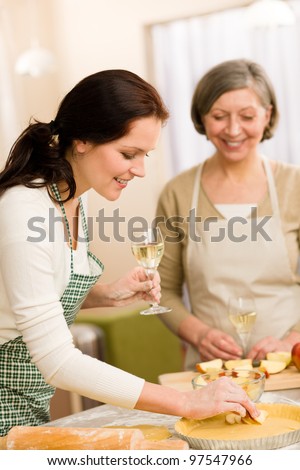 Two happy women enjoy baking apple pie drink white wine