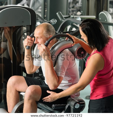 Mature man exercising at gym under supervision of personal trainer