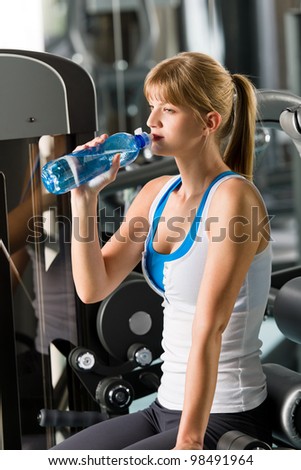 Woman drink water at the gym sitting on fitness machine