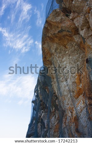 danger cliff with reinforcing net against blue sky