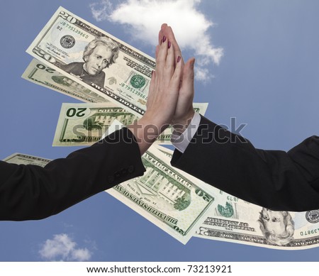 Business couple male and female high five against a blue sky that has American twenty dollar bills fluttering down