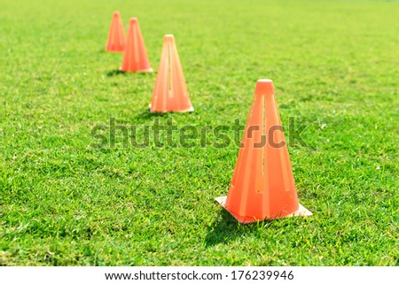 Soccer cone standing on grass in field.