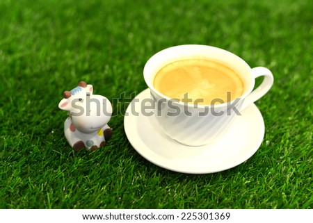 Coffee cup on the grass texture with a cow doll.