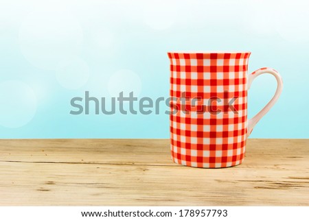 Red plaid cup on wooden table.Mug on blue background with space for text.