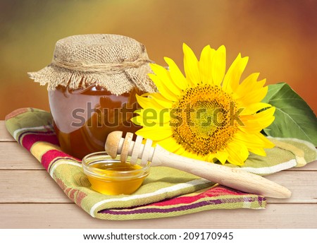 Glass bowl of honey with sunflower on wooden table.