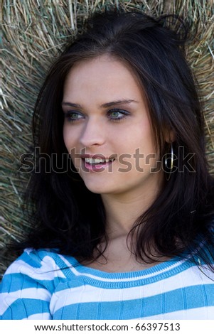 Summer portrait of a girl leaning against a bundle of straw