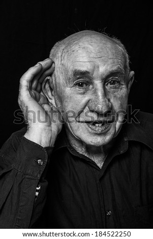 old man who hears evil, hand to ear listens isolated black background