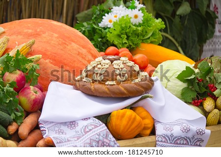 On a white towel is a beautifully decorated cake, nearby there are a variety of vegetables and fruits such as pumpkin, cabbage, apples, carrots.
