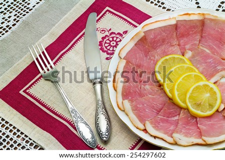 Delicious slices of ham and lemon on the plate, next Cutlery: knife and fork.