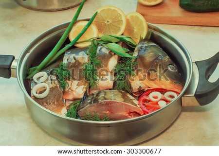 In a large skillet, stainless steel is chopped fish and ingredients for cooking: vegetables, lemon, onion, dill.