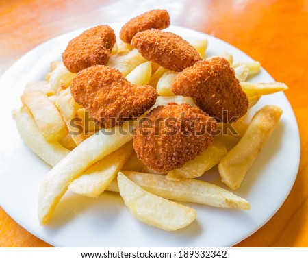 The deep fried potato chips and chicken nuggets on the white dish with the wooden table