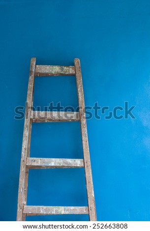 Wooden ladder with paint against blue wall