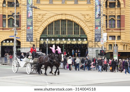 Melbourne, Australia - Aug 29, 2015: People crossing a crosswalk outside Flinders Street Railway Station in Melbourne, Australia, with a horse-drawn carriage passing by