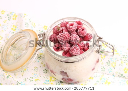 breakfast rice porridge with vanilla sauce, frozen raspberries in a glass jar white background