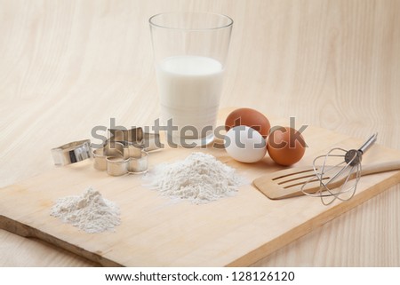 glass of milk, whisk, Cookie cutter forms and eggs on wooden table together