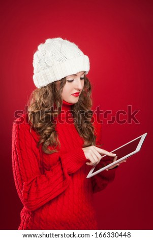 beautiful brunette girl wearing red sweater and holding tablet touches screen searing internet over red background