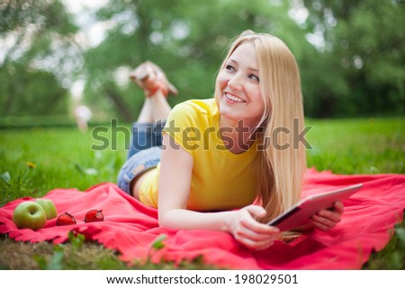 blonde girl lying in the park with tablet on the red coverlet. summer