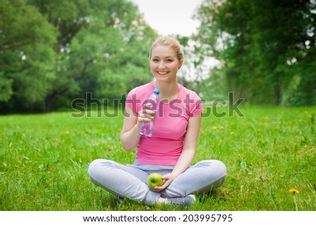 blonde girl outdoor in the park with water and apple on the grass