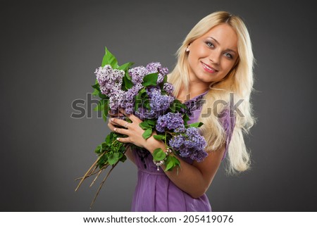 blonde girl in purple dress holding bouquet of lilac over grey background