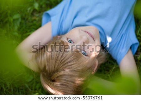 little boy in blue t-shirt lying on the grass  under tress
