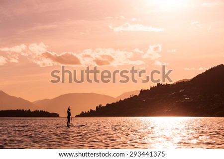 young female paddles a paddleboard off Lake Wakatipu at the sunset