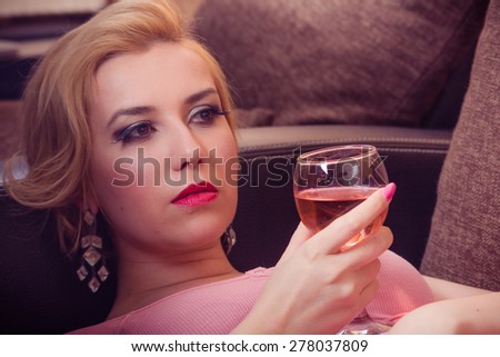 Relaxed casual blonde woman in pink cardigan holding a book lying on a dark brown couch