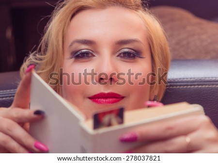 Relaxed casual blonde woman holding a book lying on a dark brown couch