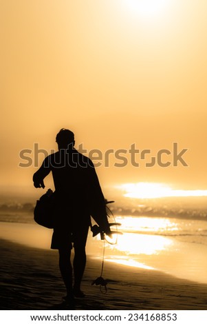 A surfer silhouette walking at the beach while the sun is setting. Photo taken in Byron Bay, Australia