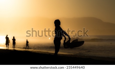 A woman's silhouette at sunset at the Byron Bay beach packing together her things to leave .