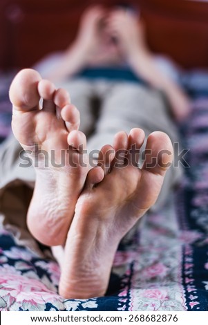 Close-up of male feet and a blurry person laying on a bed