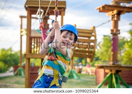 Little cute boy enjoying activity in a climbing adventure park on a summer sunny day. toddler climbing in a rope playground structure. Safe Climbing extreme sport with helmet insurance motion blurred