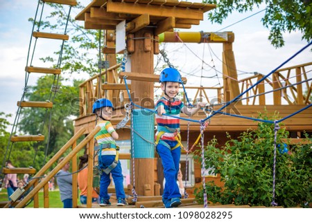 Twin brothers in helmet walks by rope at park sunny summer day in adventure playground. Active healthy leisure time spending concept with children.