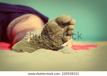Close-up of the foot of a sleeping man lying on the beach