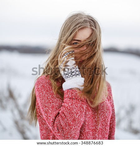 winter outdoor portrait of serious young girl with red jacket and blond fluttering hair in windy weather in natural field background. Lifestyle